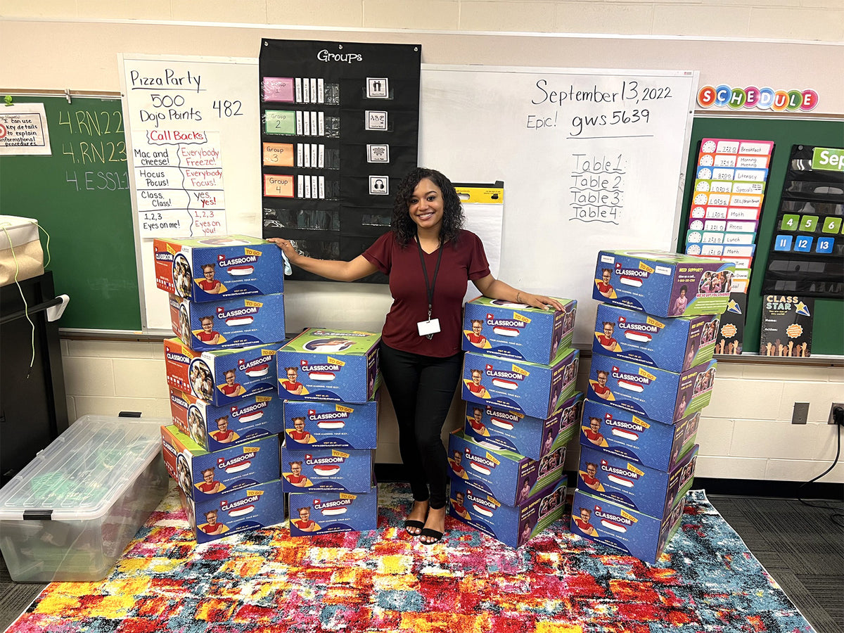 Skylar Thomas in her classroom beside the stack of Classroom TO GO kits. The photograph is in Drive: 1sq9h0yp7RzePLNpxSDHn315gB4zeenGW