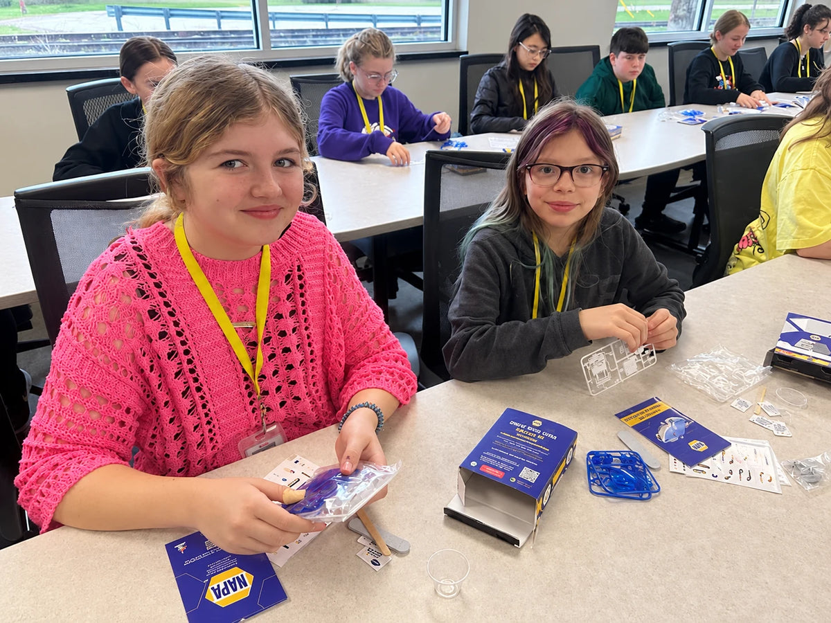 Students building Saltwater Cars at long classroom tables, with parts sprues, instruction cards and kit boxes spread out in front of them.