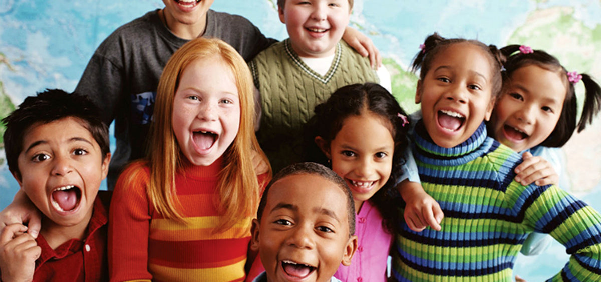 Eight school-age children of several ethnicities crowded together in front of a world map, all of them laughing and cheering at the camera.