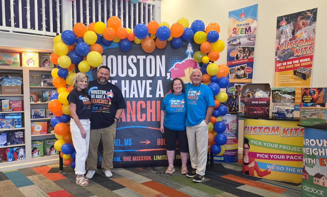 Five people standing and smiling in front of a balloon arch and a banner reading Houston, We Have a Franchise, with Central Creativity product shelving behind them.