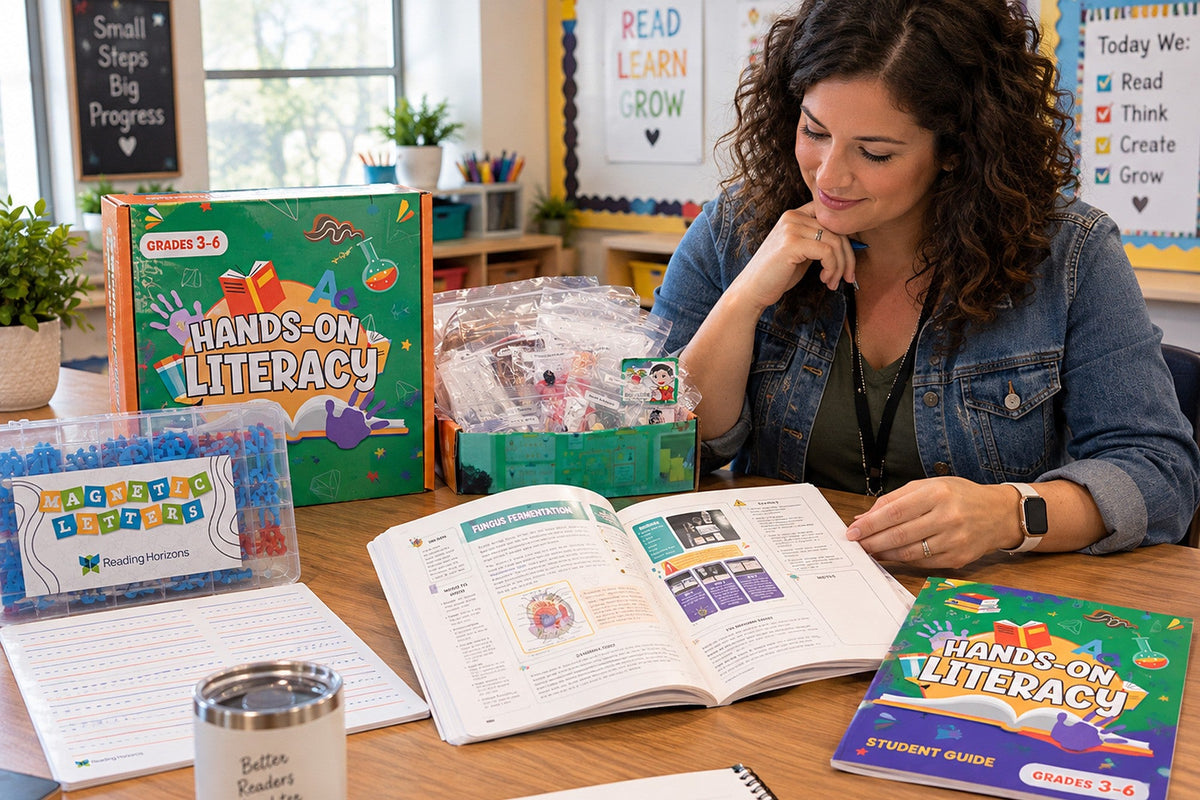 A teacher at a classroom table with the Grades 3-6 Hands-On Literacy kit open beside her, reading an activity spread in the teacher guide, magnetic letters and the student guide within reach.