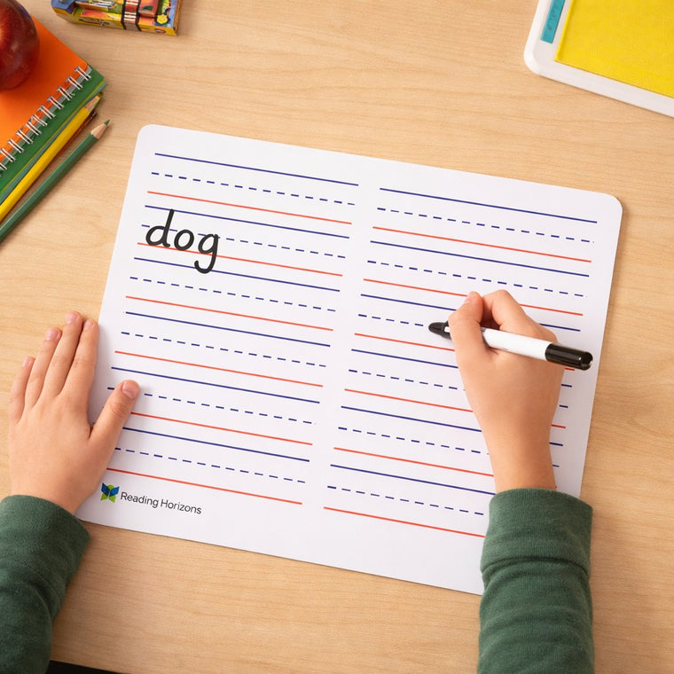 A child writing the word dog in marker on the lined Reading Horizons writing board, one hand steadying the board.