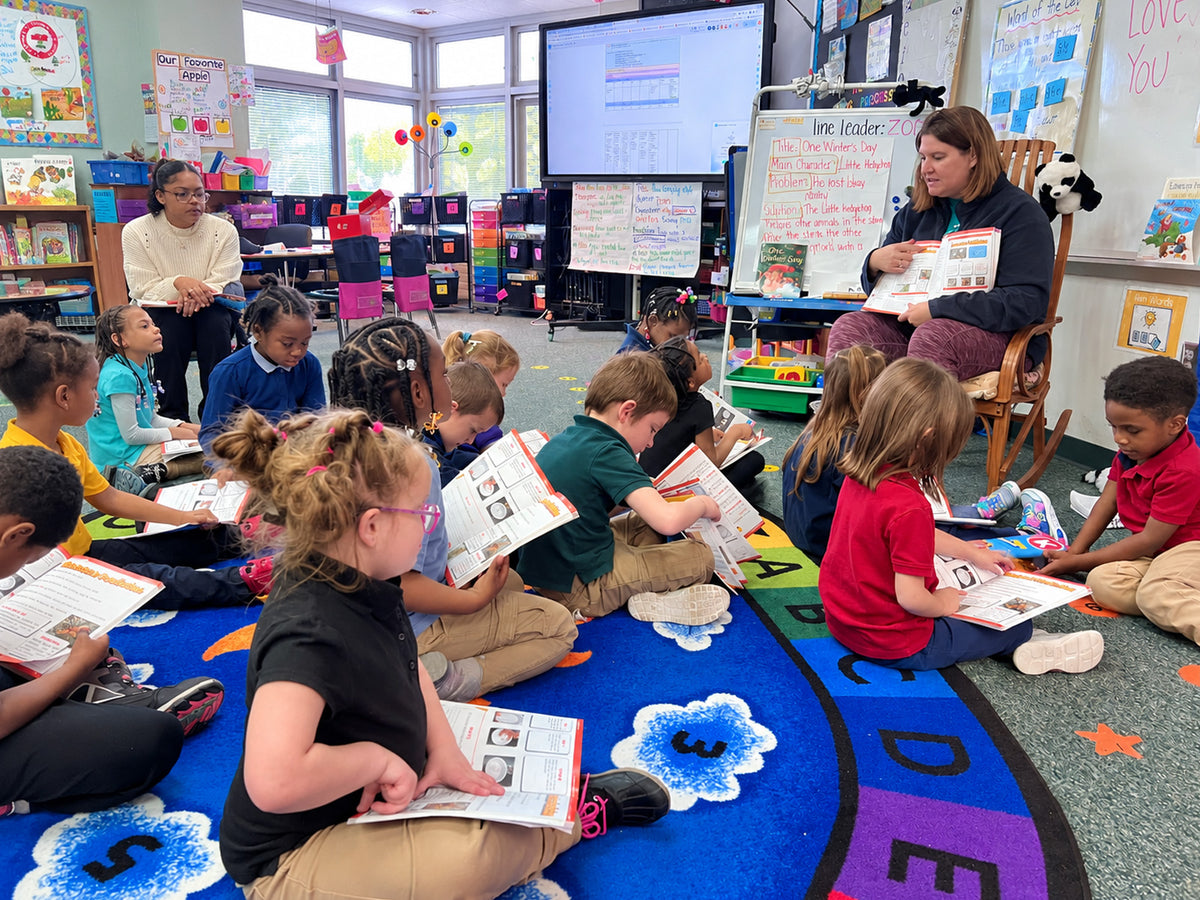 A student holding up her build and explaining it, while an instructor crouches to listen and another student leans in to argue a point.