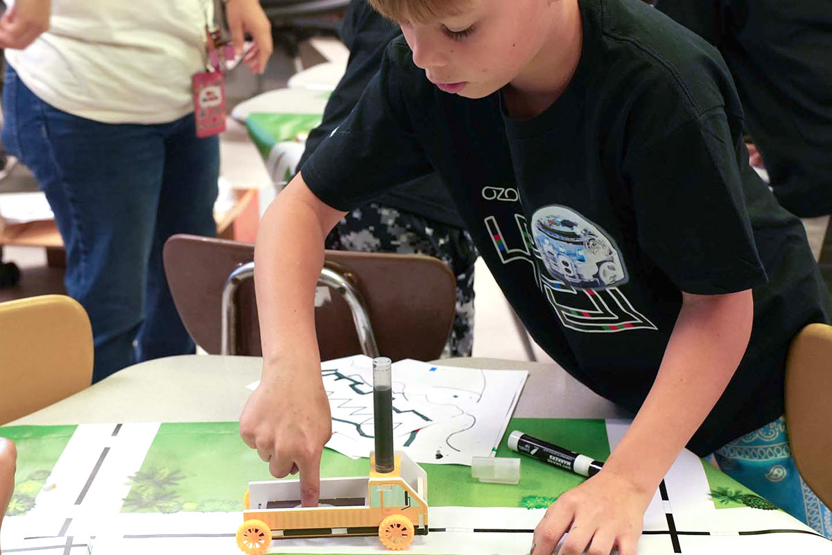 A student testing a joint on the build kit, pieces and wheels on the table.