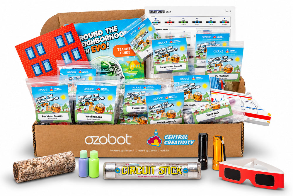 The teacher kit open on a white background: the printed Ozobot and Central Creativity box filled with labeled activity packets, the Teacher Guide and color code chart standing behind it, and the extra supplies laid out in front &mdash; a bark log, two dough bottles, the Circuit Stick, two flashlights and a pair of bee vision glasses.