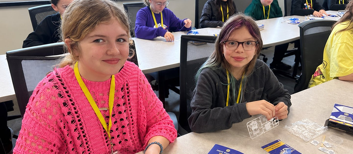 Two Litchfield Middle School students at a classroom table with Drive Into STEM kit boxes, clear parts sprues and instruction cards in front of them