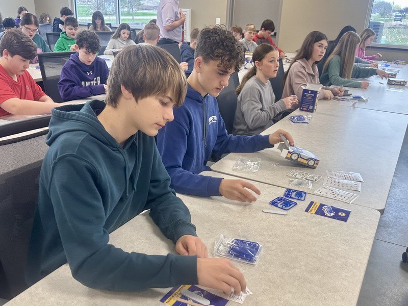 Students along a shared table opening kit packets and sorting the parts