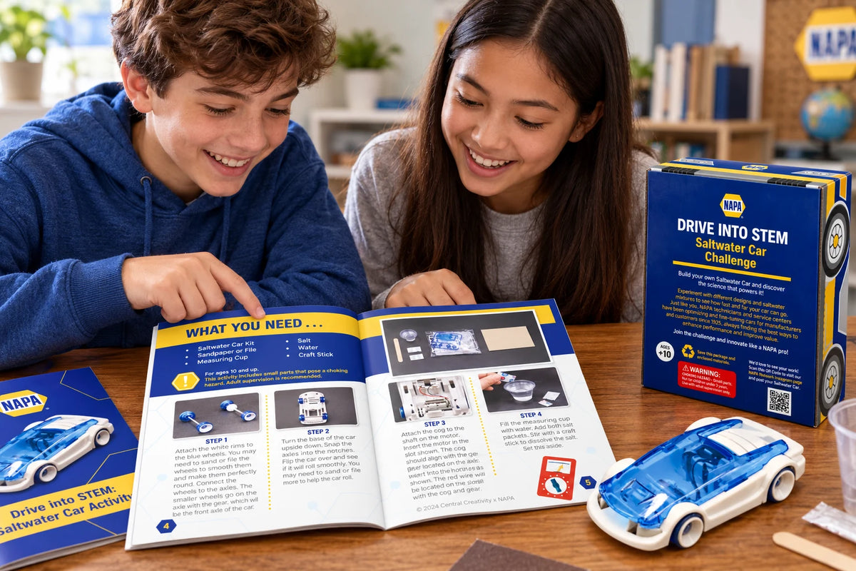 Two students at a table reading the open activity guide together, with the kit box, the finished car, a craft stick and a sanding block beside them.