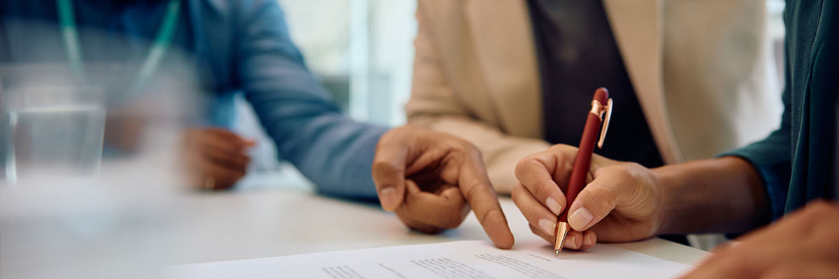 Two people at a table in close discussion over a document, one of them pointing at a line of it with a red pen.