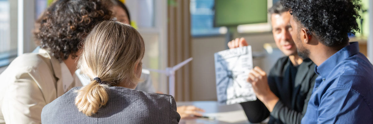 A small group at a table reviewing a printed report together, one of them holding it up so the others can see.