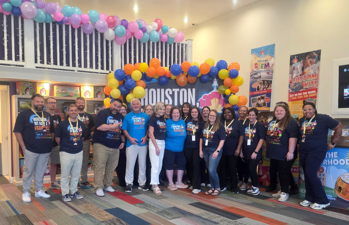 The Houston franchise owners standing with the whole Central Creativity team beneath a balloon arch in the headquarters lobby, in front of a Houston backdrop.