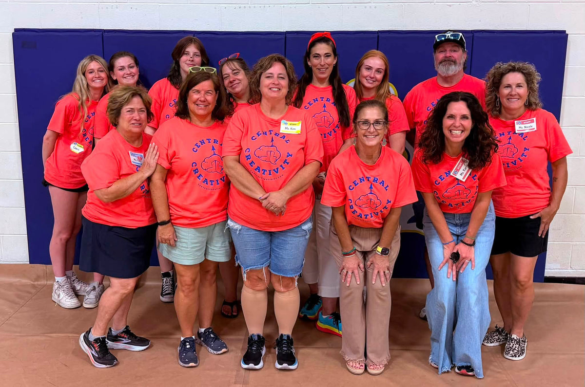 The Louisville Central Creativity team, fourteen people in matching coral shirts, standing together in a school gymnasium after an event.