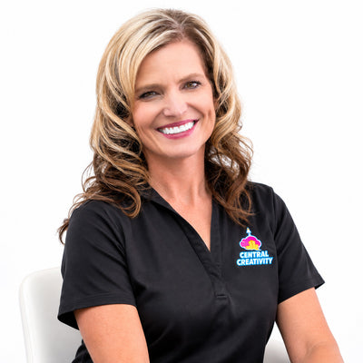 Jenny McLeod, smiling with her arms folded, wearing a black Central Creativity polo shirt against a plain light background.