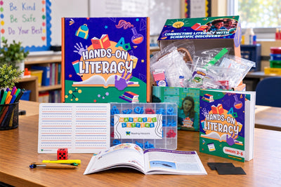 The Grades 3-6 Hands-On Literacy kit laid out on a classroom table: the printed box, a second box of bagged activity materials, the lined writing board, a case of magnetic letters, the teacher guide and an open activity spread.