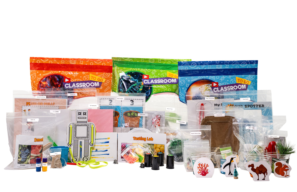 Three Classroom TO GO kit bags in orange, green and blue standing behind a wide spread of individually sealed, labeled student packets holding test tubes, colored liquids, a cut-out robot, animal figures and other activity materials.