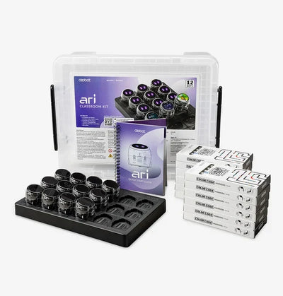 The Ari Classroom Kit for twelve: a clear lidded storage tub, the lesson folder and quick start guide, twelve Ari robots seated in a black charging tray, and a stack of Color Code marker boxes.