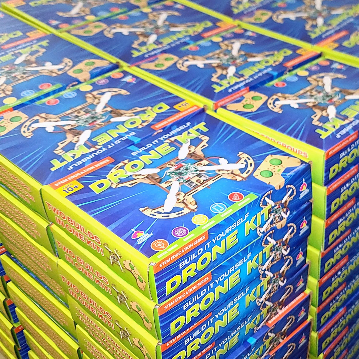 A pallet stacked with rows of Build It Yourself Drone Kit boxes, lime green and blue, each marked Ages 10 plus and Two builds in one kit